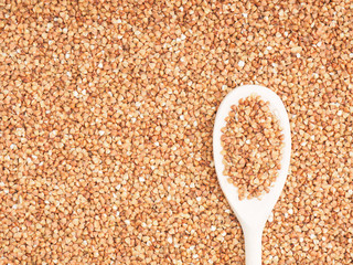 Buckwheat groats in wooden spoon on a buckwheat background. Healthy eating concept
