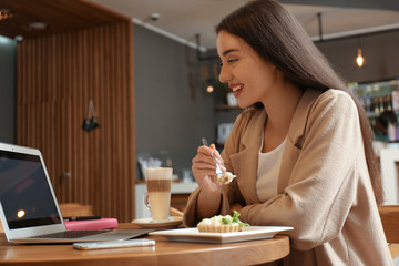 Young blogger with laptop eating cake in cafe