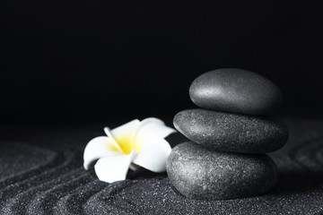 Fototapeta na wymiar Spa stones and plumeria flower on black sand with beautiful pattern, space for text. Zen concept