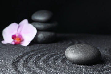 Obraz na płótnie Canvas Spa stones and orchid flower on black sand with beautiful pattern. Zen concept