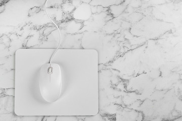 Modern wired optical mouse and pad on white marble table, top view. Space for text