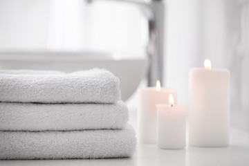 Stack of fresh towels and burning candles on countertop in bathroom