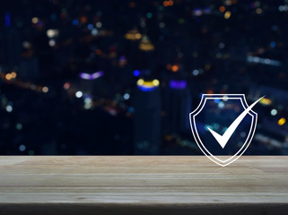 Fototapeta na wymiar Security shield with check mark flat icon on wooden table over blur colorful night light modern city tower and skyscraper, Technology internet cyber security and anti virus concept