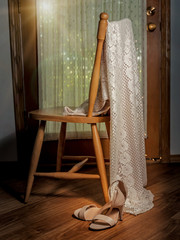 A wedding dress and matching pair of shoes draped carefully over the back of a wooden chair. 