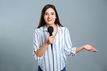 Young female journalist with microphone on grey background