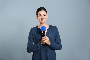 Young female journalist with microphone on grey background