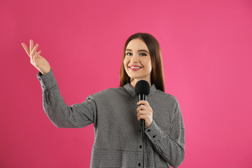 Young female journalist with microphone on pink background