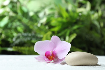 Fototapeta na wymiar Stone and beautiful flower on sand against blurred green background. Zen, meditation, harmony
