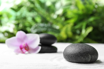 Fototapeta na wymiar Dark stones and beautiful flower on sand against blurred green background. Zen, meditation, harmony