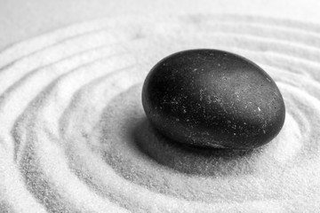 Fototapeta na wymiar Black stone on sand with pattern. Zen, meditation, harmony