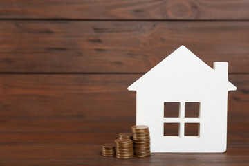 House model and coins on wooden background. Space for text