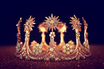 low key image of beautiful queen/king crown over gold glitter table. vintage filtered. fantasy medieval period