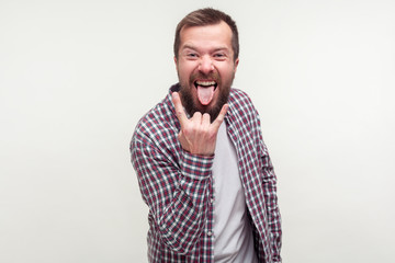 Portrait of crazy optimistic bearded man in plaid shirt showing rock and roll sign hand gesture and...