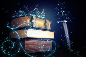 low key image of beautiful queen/king crown over antique book and sword. fantasy medieval period....