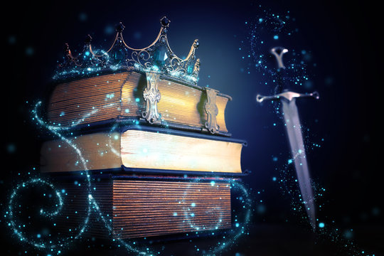 low key image of beautiful queen/king crown over antique book and sword. fantasy medieval period. Selective focus