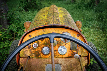 Fototapeta na wymiar Old desolate rusty Italian tractor in the forest - view at dashboard against green grass. Middle of XX century machinery out of processing - symbol of past relic technology. Vintage background.