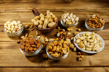 Assortment of nuts on wooden table. Almond, hazelnut, pistachio, peanut, walnut and cashew in small bowls. Healthy eating concept