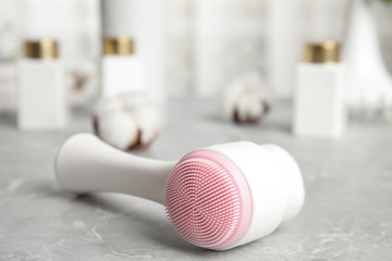 Modern face cleansing brush on light grey marble table. Cosmetic accessory