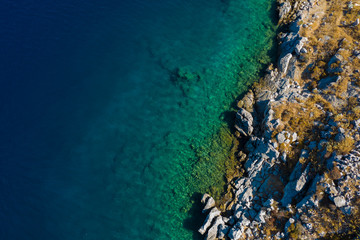 Aerial top view of sea waves hitting rocks on the beach with turquoise sea water. Amazing rock cliff seascape in Greece coastline. Drone shot.