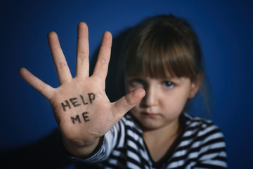 Abused little girl showing with phrase HELP ME near blue wall, focus on hand. Domestic violence concept