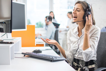 Happy female call center operator in headset making video call to business partner using computer...