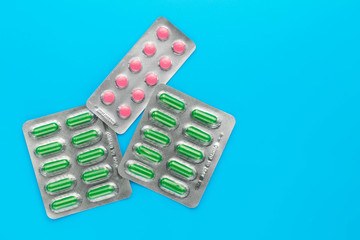 Pack of pills on a blue background. Copy space. Blisters of pink tablets and green capsules. Medicine concept.