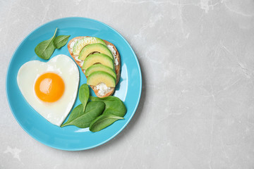 Romantic breakfast with heart shaped fried egg on light grey table, top view. Space for text