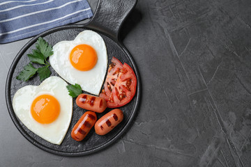 Delicious breakfast with heart shaped fried eggs and  sausages served on dark grey table, flat lay....
