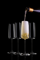 Four glasses of champagne on dark background. A full glass of champagne in the middle. From above poured champagne from the bottle.