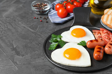 Delicious breakfast with heart shaped fried eggs and sausages on dark grey table. Space for text