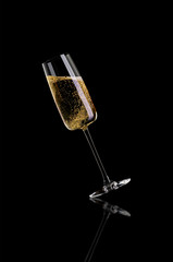 A glass of champagne, without the foam on a dark background is tilted to the left.