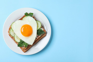 Plate of tasty sandwich with heart shaped fried egg on light blue background, top view. Space for text