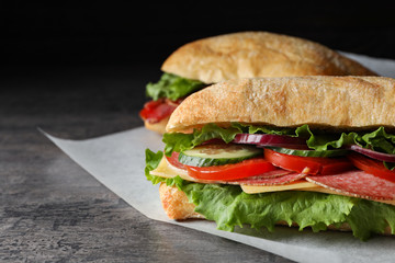 Delicious sandwiches with fresh vegetables and salami on grey table, closeup