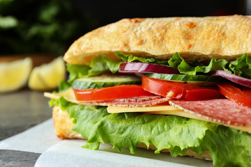 Delicious sandwich with fresh vegetables and salami on grey table, closeup