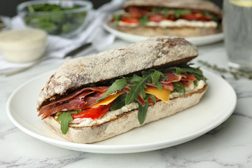 Delicious sandwich with fresh vegetables and prosciutto on white marble table