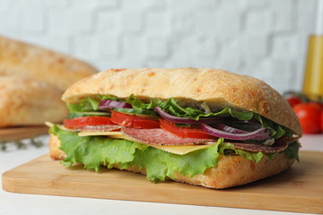 Delicious sandwich with fresh vegetables and salami on white table