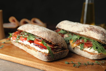 Delicious sandwiches with fresh vegetables and prosciutto on table