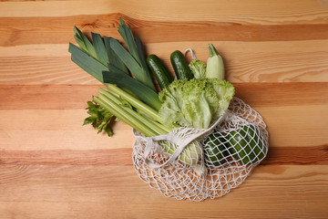 White net bag with vegetables on wooden background, top view