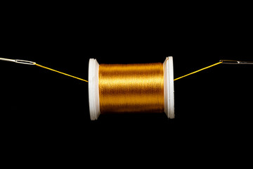 A spool of gold thread suspended on a field of black on a thread between 2 needle eyes.  Plenty of...