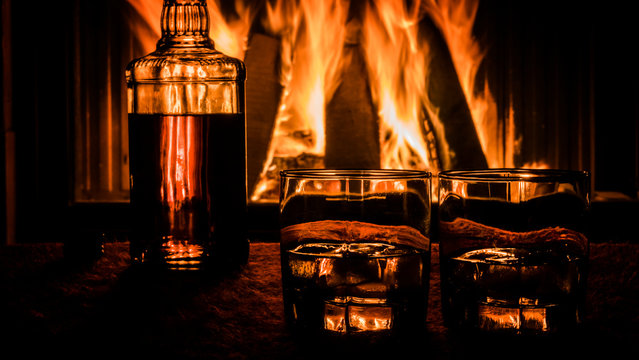 Closeup shot of Two glasses and a bottle of whiskey stand on the table against the background of a hot fireplace
