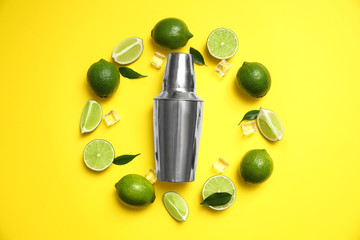 Flat lay composition with fresh juicy limes, ice cubes and cocktail shaker on yellow background
