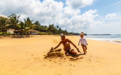 Fototapeta na wymiar happy healthy family father and daughter building sand castle on beach smiling and carefree.
