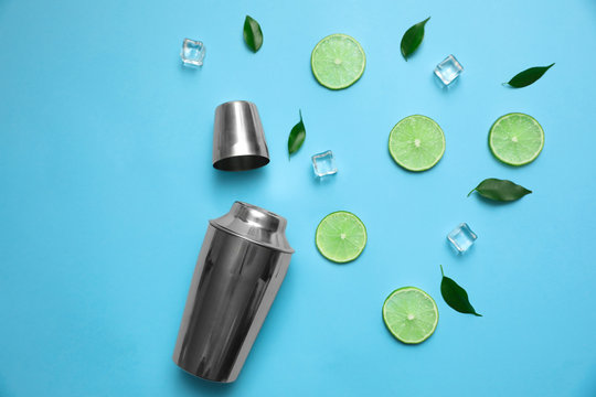 Flat lay composition with fresh juicy limes, ice cubes and cocktail shaker on light blue background