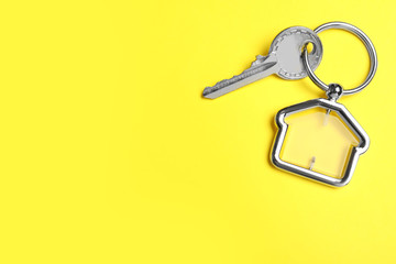 Key with trinket in shape of house on yellow background, top view and space for text. Real estate agent services