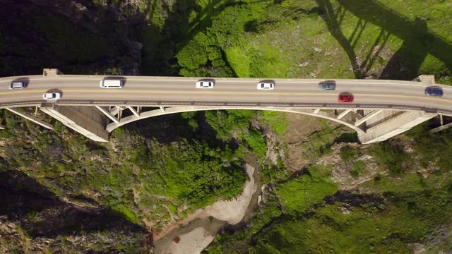 Topdown aerial view over the cars driving the Bixby Creek Bridge. The construction built over the canyon between two mountains. Very popular arch bridge because of its beauty and location. 4K