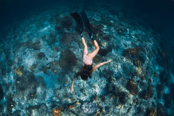 Freediver girl with fins glides over sandy bottom with fishes in blue ocean