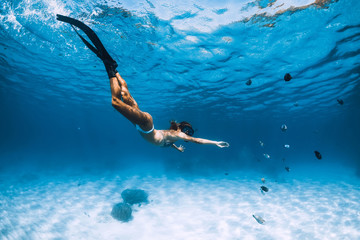Freediver girl with fins glides over sandy bottom with fishes in blue ocean © artifirsov