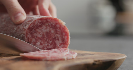 man slicing salame sausage on olive wood board