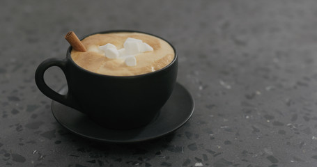 cappuccino with marshmallow and cinnamon in black cup on terrazzo countertop