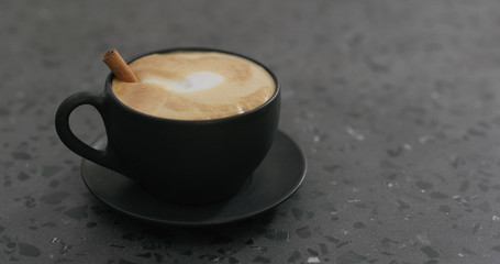 cappuccino with marshmallow and cinnamon in black cup on terrazzo countertop